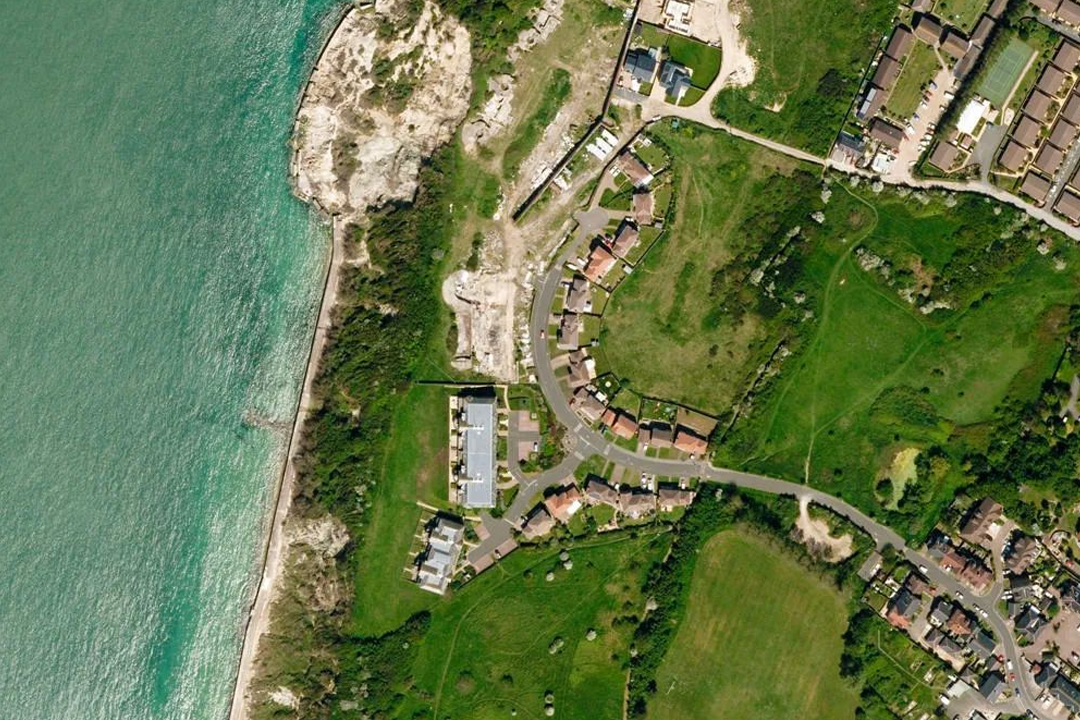 Close-up OS aerial imagery showing a coastal settlement - beach, rocky shoreline, golf course, houses and roads in true top-down orthorectified view